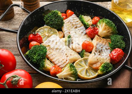 Morue savoureuse cuite avec des légumes dans une poêle à frire sur une table en bois Banque D'Images