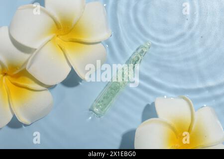 Ampoule de soin de la peau et belles fleurs de plumeria dans l'eau sur fond bleu clair, pose plate Banque D'Images