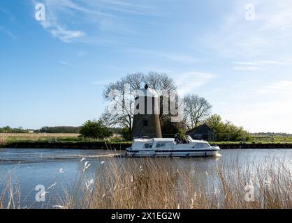 Upton, Norfolk, Royaume-Uni – 14 avril 2024. Location de bateau passant devant un moulin désaffecté sur la rivière Bure, Norfolk Broads Banque D'Images