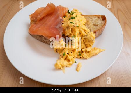 Oeufs brouillés saupoudrés de ciboulette sur pain grillé au levain avec saumon fumé sur une assiette blanche. Banque D'Images