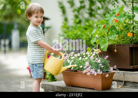 Mignon petit garçon arrosant des parterres de fleurs dans la cour arrière le jour d'été. Enfant utilisant l'arrosoir pour arroser les plantes. Enfant aidant avec les corvées quotidiennes. Maman Banque D'Images