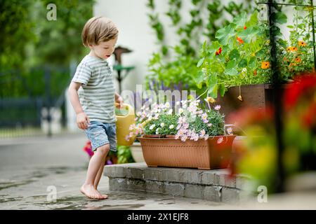 Mignon petit garçon arrosant des parterres de fleurs dans la cour arrière le jour d'été. Enfant utilisant l'arrosoir pour arroser les plantes. Enfant aidant avec les corvées quotidiennes. Maman Banque D'Images