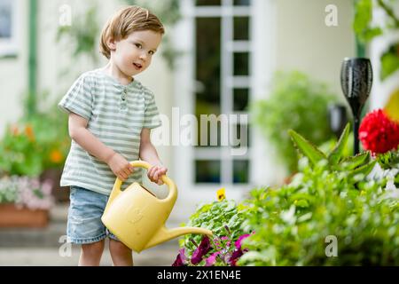 Mignon petit garçon arrosant des parterres de fleurs dans la cour arrière le jour d'été. Enfant utilisant l'arrosoir pour arroser les plantes. Enfant aidant avec les corvées quotidiennes. Maman Banque D'Images