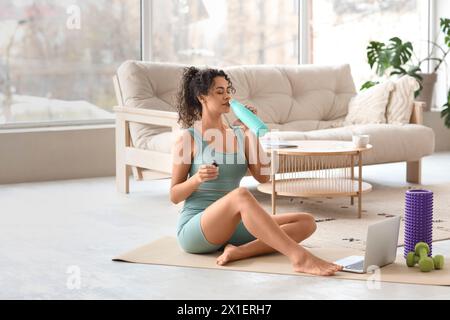 Jeune femme sportive afro-américaine buvant de l'eau après un entraînement à domicile Banque D'Images