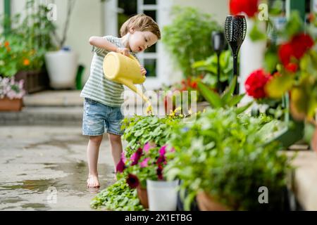 Mignon petit garçon arrosant des parterres de fleurs dans la cour arrière le jour d'été. Enfant utilisant l'arrosoir pour arroser les plantes. Enfant aidant avec les corvées quotidiennes. Maman Banque D'Images