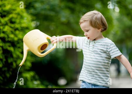 Mignon petit garçon arrosant des parterres de fleurs dans la cour arrière le jour d'été. Enfant utilisant l'arrosoir pour arroser les plantes. Enfant aidant avec les corvées quotidiennes. Maman Banque D'Images