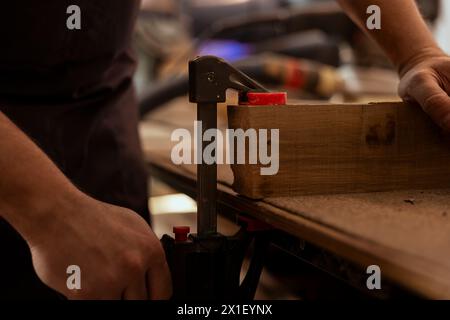 Menuisier utilisant un étau d'établi pour maintenir le bloc de bois, commencer l'assemblage des meubles en atelier, plan rapproché. Fabricant dans la menuiserie en utilisant l'outil étau pour saisir le morceau de bois avant de le sculpter Banque D'Images