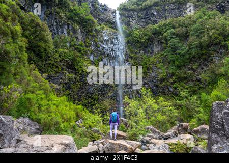 Description : femme touriste avec sac à dos profite de l'atmosphère à la chute d'eau tombant de haut mur de roche. Cascade de Lagoa do Vento, île de Madère, Portug Banque D'Images