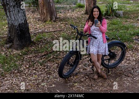 Jeune femme latino-américaine (33 ans) en balade printanière avec son vélo électrique, elle utilise son téléphone portable. Concept de moyen de transport et de ressort. Banque D'Images