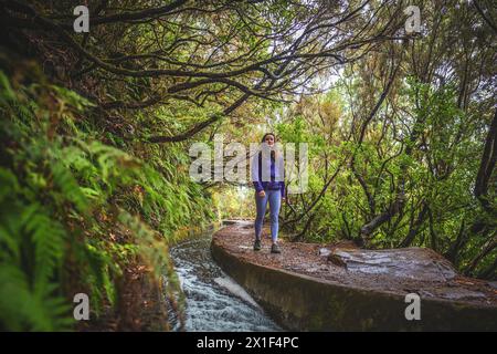 Description : femme touriste avec sac à dos marchant le long d'un canal d'eau courbe et en pente envahi par des arbres lauraux un jour de pluie. 25 Fontes Waterfal Banque D'Images