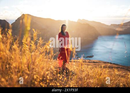 Description : femme heureuse en robe rouge profite de l'atmosphère matinale sur les contreforts d'une île volcanique dans l'océan Atlantique. São Lourenço, Madère Banque D'Images