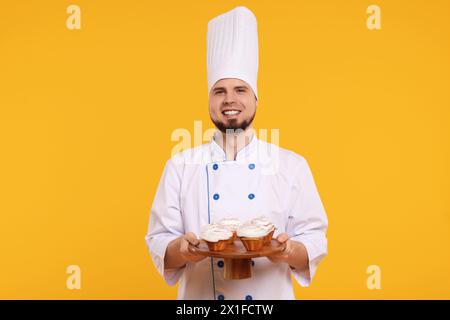 Heureux confiseur professionnel en uniforme tenant de délicieux cupcakes sur fond jaune Banque D'Images