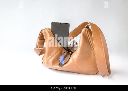 Sac à main en cuir femme avec téléphone et lunettes. Sur fond blanc, copier l'espace. Banque D'Images