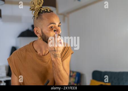 Noir gay brésilien appliquant maquillage ombre à paupières regardant miroir vue de derrière. Gars non binaire. LGBT mode de vie lgbtq concept Banque D'Images