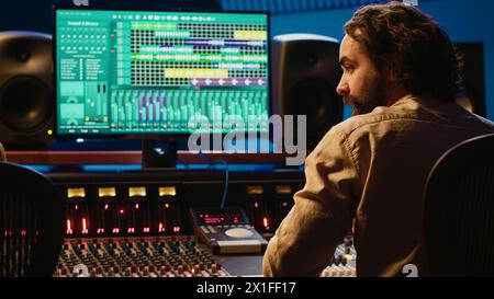 Équipe d'artiste et de technicien éditant l'audio après la session d'enregistrement dans la salle de contrôle, mixage et mastering des pistes sur la console dans la salle de contrôle. Appuyer sur les boutons et appuyer sur les curseurs. Caméra A. Banque D'Images