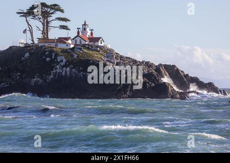 Un phare se trouve sur une colline rocheuse. Le phare est blanc et rouge, et il est entouré par une colline verdoyante. La scène est paisible et sereine Banque D'Images