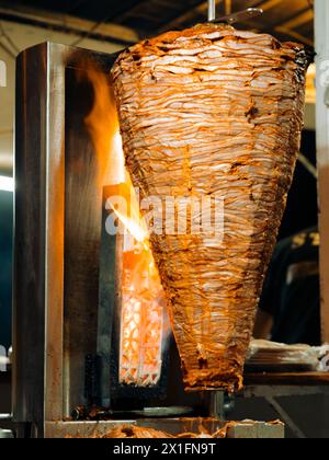 Image verticale griller traditionnel trompo al Pastor Street taco viande de porc sur la broche avec des flammes la nuit au Mexique. Banque D'Images