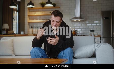 Homme assis sur le canapé à l'aide de smartphone vérifier le message de lecture avis recevoir de bonnes nouvelles sur l'e-mail célébrer la grande opportunité se sent heureux Banque D'Images