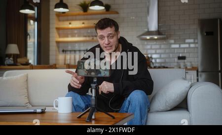 Influenceur vlogger homme assis sur le canapé enregistrement vidéo blog sur la caméra mobile trépied parler pour canal multimédia personnel, streaming session en direct blog Banque D'Images