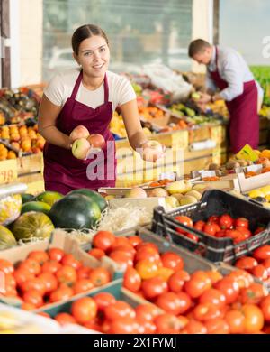 Sympathique vendeuse offrant des pommes mûres dans le magasin de fruits et légumes Banque D'Images