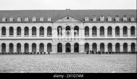 Les visiteurs traversent la cour pavée des Invalides sous un ciel couvert de Paris, France. Image en noir et blanc. Banque D'Images