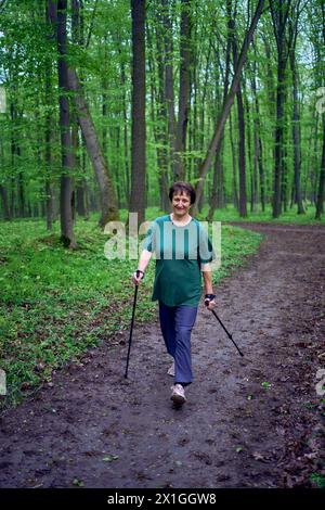 Une femme âgée est engagée dans la marche nordique avec des bâtons dans la forêt de printemps Banque D'Images