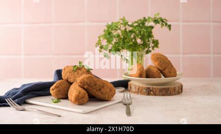 Boulettes de morue, ou « bolinhos de bacalhau » et feuilles de persil sur des plats en céramique blanche dans un comptoir de cuisine. Banque D'Images