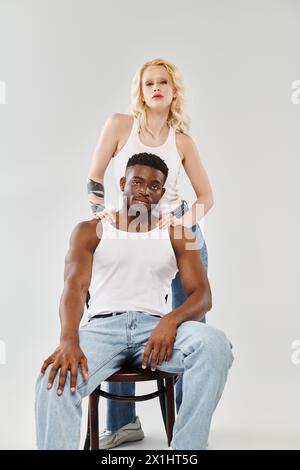 Un homme assis au sommet d'une chaise engage une conversation avec une femme à côté de lui dans un cadre de studio sur un fond gris. Banque D'Images