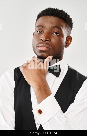 Beau jeune marié afro-américain portant un gilet noir et noeud papillon dans un cadre de studio sur un fond gris. Banque D'Images