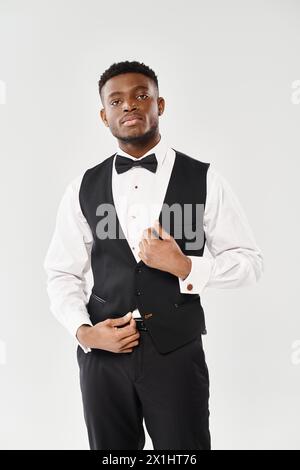 Un jeune homme afro-américain dans un élégant smoking frappe une pose sophistiquée pour un portrait sur un fond gris de studio. Banque D'Images