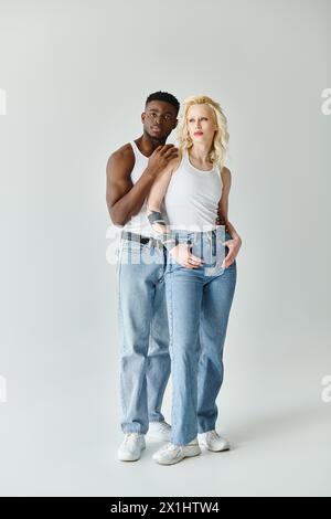Un jeune couple multiculturel debout ensemble dans un studio sur un fond gris, mettant en valeur l’unité et la diversité. Banque D'Images