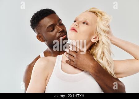 Un homme se tient à côté d'une femme dans un débardeur blanc dans un cadre de studio avec un fond gris. Banque D'Images