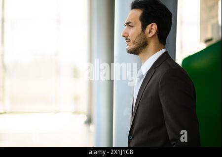 Homme professionnel en costume regarde par une fenêtre, perdu dans ses pensées Banque D'Images