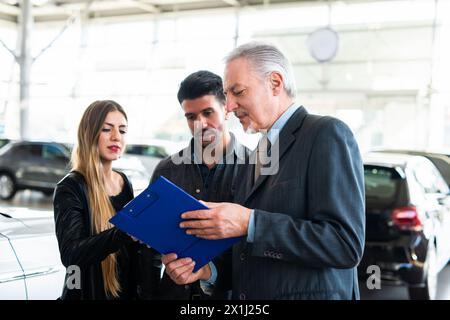 Jeune famille heureuse de parler au vendeur et le choix de leur nouvelle voiture dans un showroom Banque D'Images