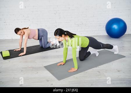 Deux femmes sur des tapis de yoga faisant des pompes, dont une enceinte, recevant les conseils d'un entraîneur pendant les cours des parents. Banque D'Images