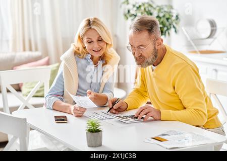 Un couple aimant mature dans des vêtements de maison confortables assis ensemble à une table, profitant d'un moment de calme ensemble dans leur cuisine à la maison. Banque D'Images