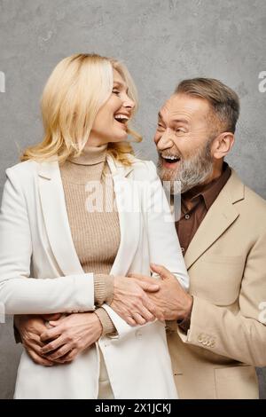 Homme et femme matures, élégamment habillés, posent l'un à côté de l'autre d'une manière aimante sur un fond gris. Banque D'Images