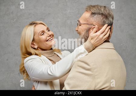 Un homme mature et une femme dans une tenue élégante embrassent avec amour sur un fond gris. Banque D'Images