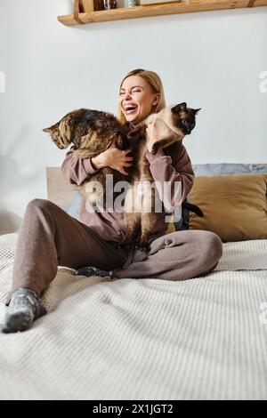 Une femme aux cheveux courts s'assoit paisiblement sur un lit, tenant deux chats près d'elle. Banque D'Images