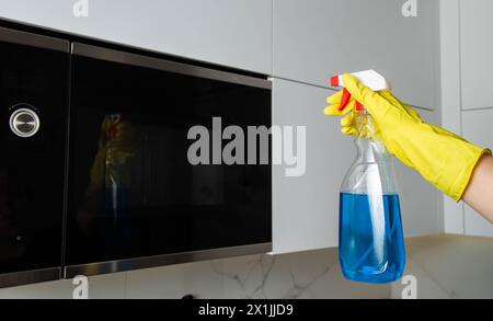 Spray anti-graisse dans la main d'une fille qui nettoie la cuisine. Nettoyer le four à micro-ondes de la graisse et de la saleté. Agent antistatique moderne. Banque D'Images