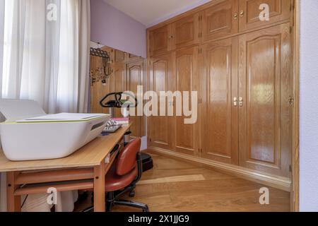 Dressing classique avec une grande armoire encastrée avec portes en chêne, bureau assorti, grand miroir sur un mur et murs peints en violet clair. Banque D'Images