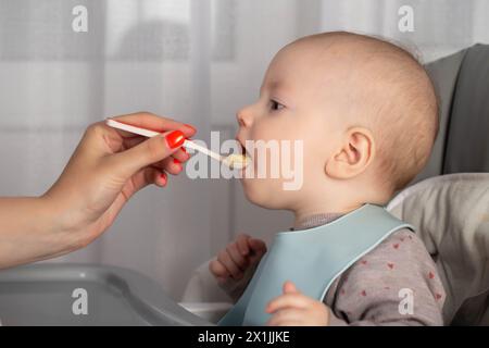 Une mère donne de la bouillie à partir d'une cuillère à un petit garçon de 8 mois. Nourrir les nourrissons. Gros plan Banque D'Images