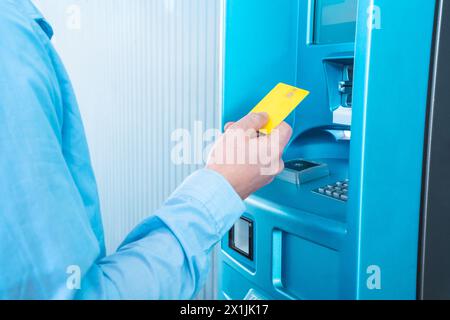 Un homme insère une carte plastique bleue dans la machine Banque D'Images