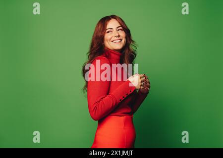 Femme tendance des années 20 dans un fond de studio vert vibrant, portant des vêtements décontractés et un pull élégant. Arborant un anneau de nez et de septum, elle exsude carefr Banque D'Images