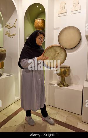 Une jeune femme iranienne montre comment jouer daf, un tambour à cadre moyen-oriental, au Musée de la musique d'Ispahan. Ispahan, Iran. Banque D'Images