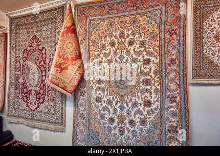 Une sélection de tapis persans en soie affichés sur un mur dans un magasin de tapis. Ispahan, Iran. Banque D'Images