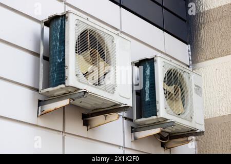 Deux climatiseurs sont fixés sur la façade en brique du bâtiment, l'un à côté d'une fenêtre et l'autre au-dessus d'un rectangle en matériau composite Banque D'Images