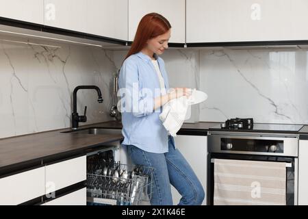 Belle femme essuyant la plaque près du lave-vaisselle ouvert dans la cuisine Banque D'Images