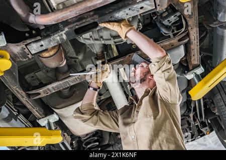 Mécanicien automobile caucasien professionnel effectuant la réparation de train de roulement Banque D'Images