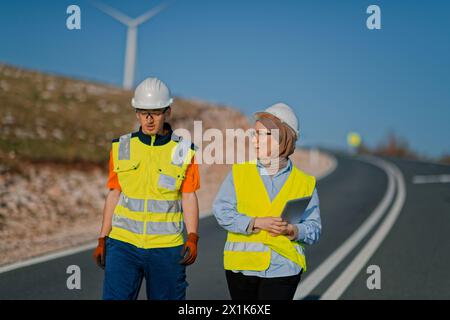 Une ingénieure avec une tablette et son collègue inspectent les éoliennes dans un champ, démontrant le travail d’équipe et le dévouement aux projets d’énergie renouvelable Banque D'Images